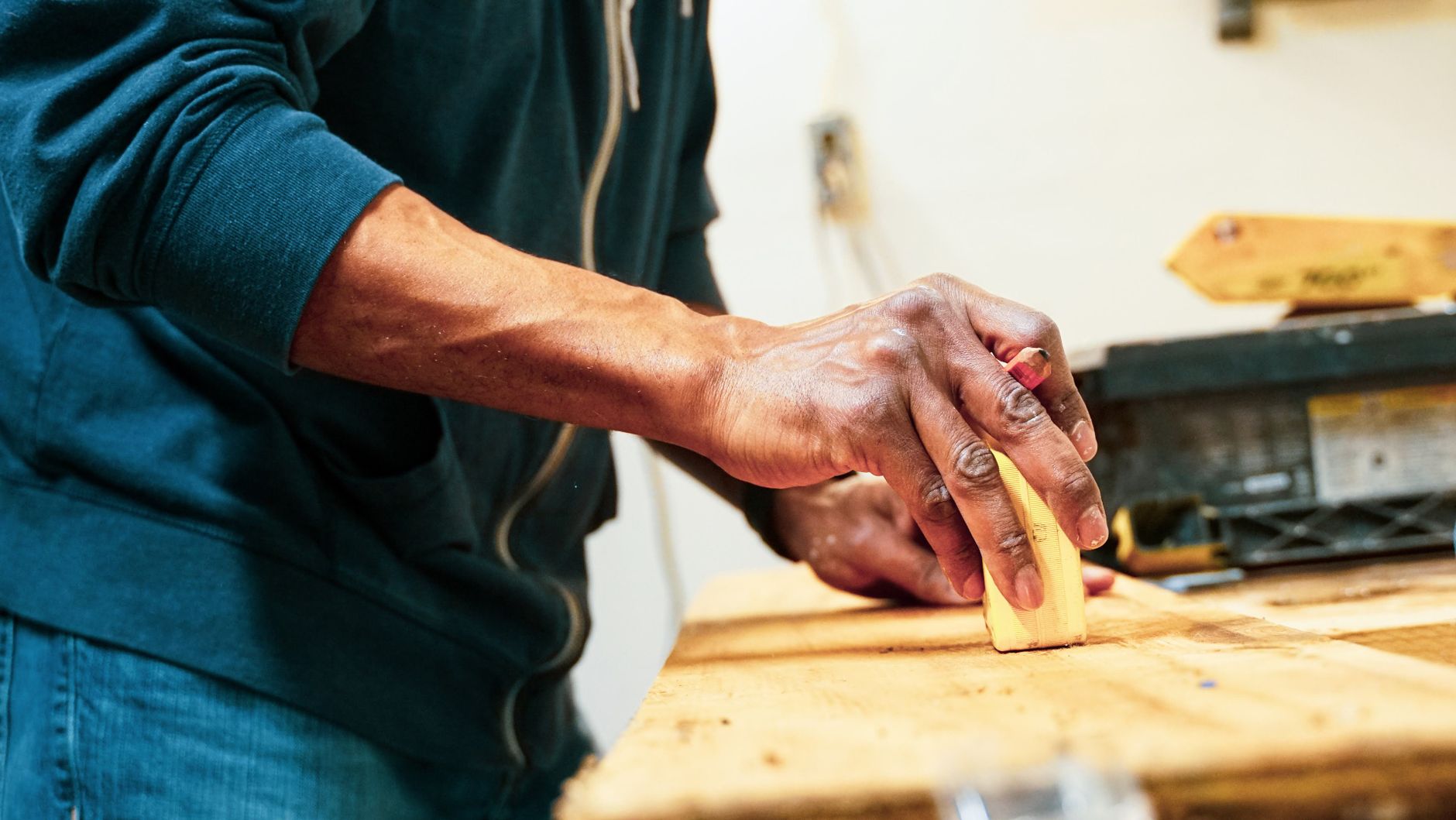 Hand schleift eine Massivholzoberfläche in der Werkstatt - Streiflicht auf der Maserung.